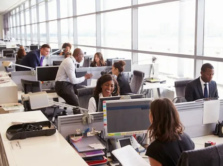 Open-plan office with staff across many desks, phones and monitors — a real-world view of operational capacity